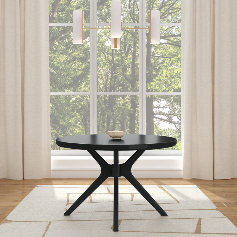 Black round dining table with modern tripod pedestal base in a contemporary dining room, beige curtains, area rug and large window with green forest view