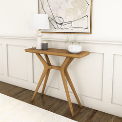 Mid-century modern wooden entryway console table with Y-shaped cross-leg base, styled with white lamp, candle, wine glasses and decorative bowl against white wainscoting