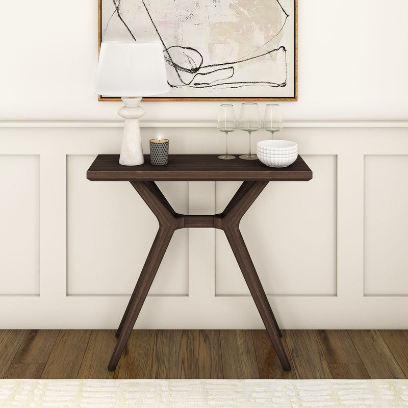 Dark wood modern console table in entryway with white lamp, lit candle, three wine glasses, ceramic bowl and abstract wall art