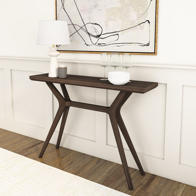 Modern dark wood console table in an entryway styled with a white ceramic table lamp, lit candle, three wine glasses and stacked white bowls beneath abstract framed wall art — minimalist home decor and entryway styling on hardwood floors with wainscoting