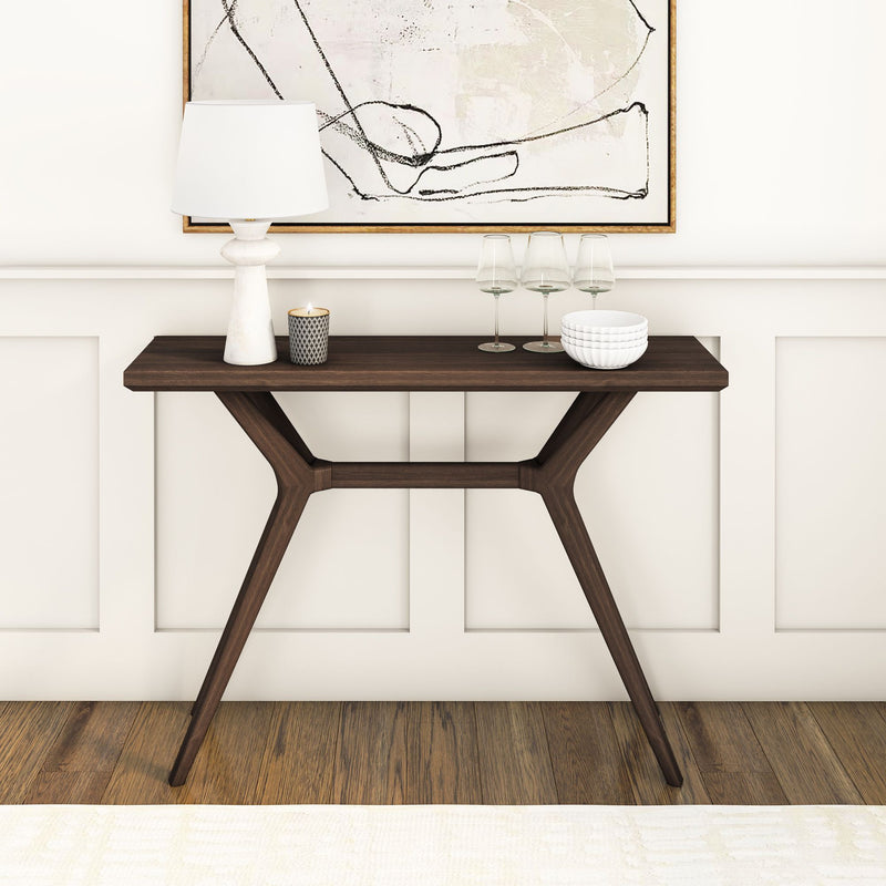 Modern wooden console table styled with white lamp, lit candle, three wine glasses, stacked white bowls and framed abstract art on a neutral paneled wall over hardwood floor