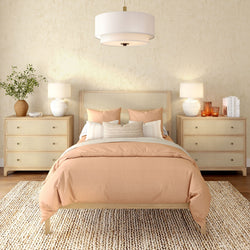 Neutral boho bedroom with blush duvet and pillows, rattan headboard, matching light-wood nightstands with lamps, pendant light and woven jute rug