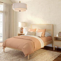 Modern boho neutral bedroom with peach duvet, wooden platform bed and rattan headboard, bedside tables with lamp, jute rug, sheer curtains and textured plaster walls