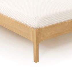 Close-up of white quilted mattress corner on a light wood platform bed frame, showing textured mattress cover and clean modern bedroom furniture design