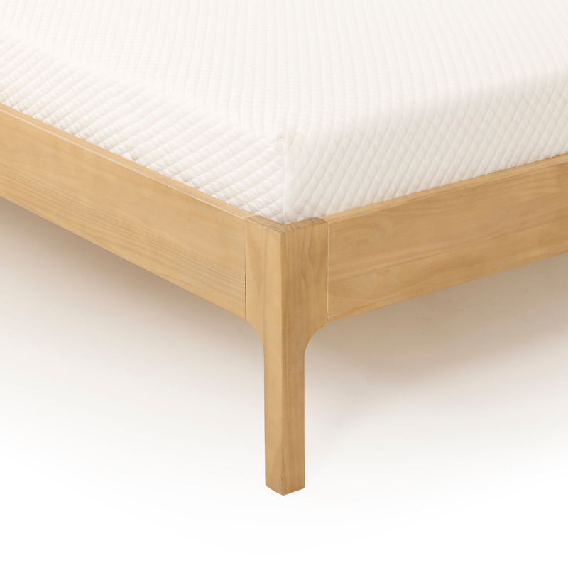 Close-up of white quilted mattress corner on a light wood platform bed frame, showing textured mattress cover and clean modern bedroom furniture design