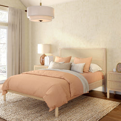 Cozy modern boho bedroom with peach bedding, rattan headboard, woven jute rug, beige textured walls, linen curtains, bedside lamp and pendant light