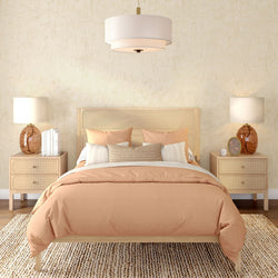 Neutral boho bedroom with peach duvet, cane headboard, light wood nightstands, amber glass lamps, woven jute rug and pendant light