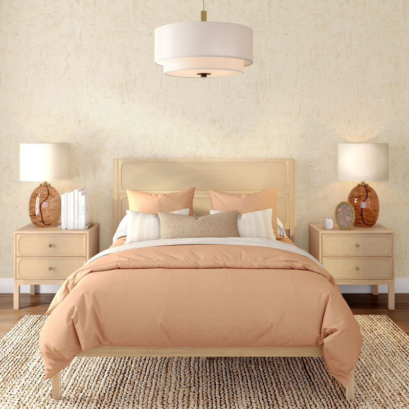 Neutral boho bedroom with peach duvet, cane headboard, light wood nightstands, amber glass lamps, woven jute rug and pendant light
