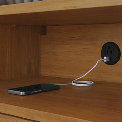 Smartphone charging inside a wooden nightstand cabinet with a round built-in USB wall outlet and white charging cable