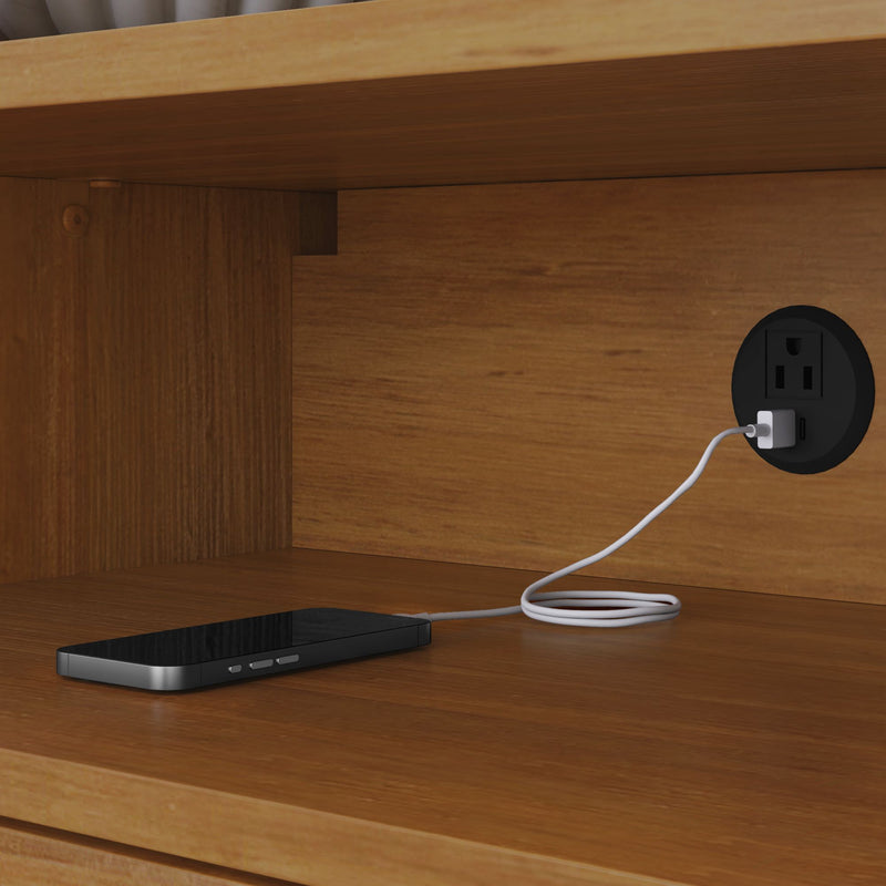 Smartphone charging inside a wooden nightstand cabinet with a round built-in USB wall outlet and white charging cable