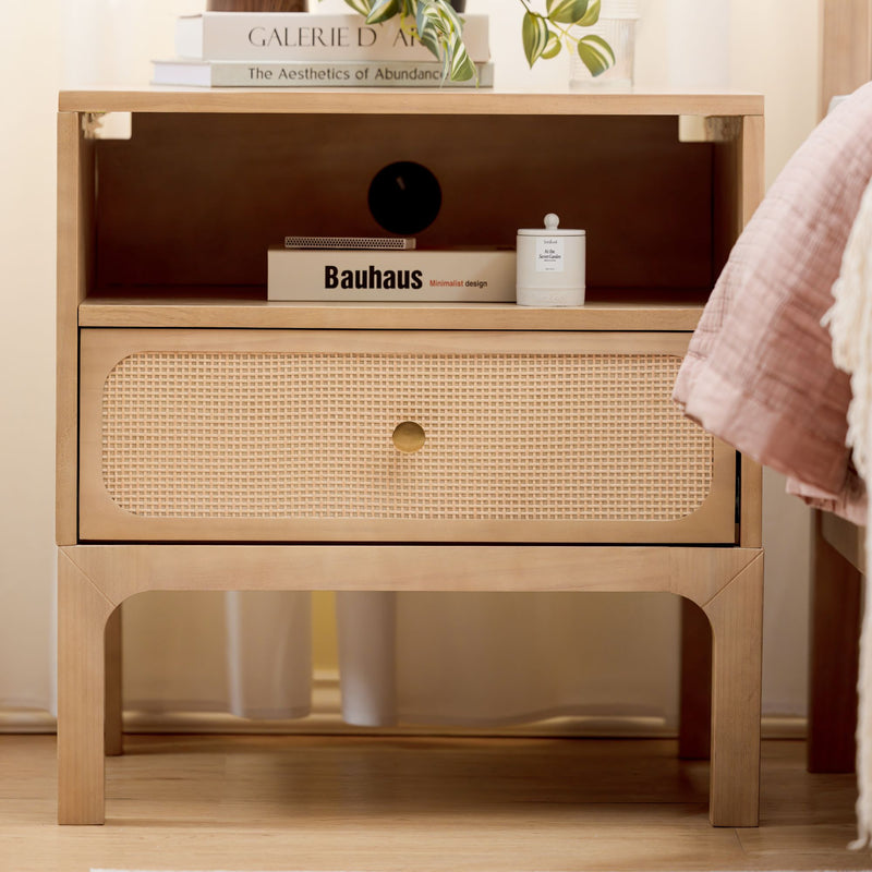 Light wood rattan-front bedside table nightstand with drawer styled in a minimalist bedroom featuring a Bauhaus book, small white candle, green plant and pink quilt