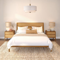 Modern boho bedroom with rattan headboard and wooden bed frame, white linens, textured jute rug, matching bedside tables with lamps and pendant light, neutral minimalist interior