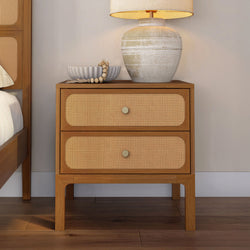 Mid-century modern rattan cane two-drawer wooden nightstand with ceramic bedside lamp and decorative bowl in styled bedroom decor
