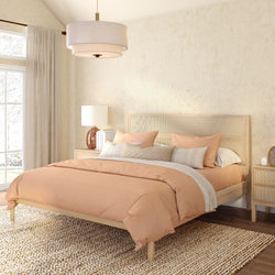 Bright modern boho bedroom with peach duvet on wooden platform bed, rattan headboard, textured cream walls, woven jute rug, matching nightstands, pendant light and natural window light.