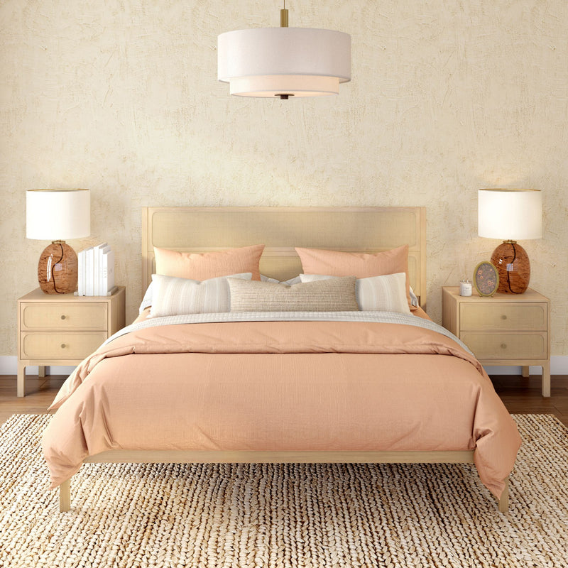 Cozy modern boho bedroom with peach duvet, rattan headboard, woven jute rug, matching nightstands and table lamps