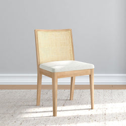 Elegant wooden chair with light upholstery on a textured rug in a minimalist room setting.