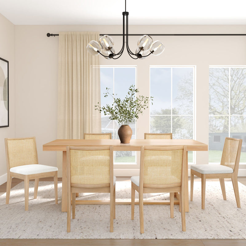 Modern Scandinavian dining room with light wood rectangular table and rattan-back chairs, glass globe pendant light, beige curtains, area rug, large windows and a clay vase of greenery flooded with natural light