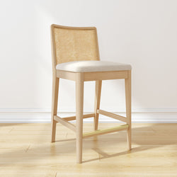 Contemporary wooden bar stool with cushioned seat and cane backrest on light hardwood floor.
