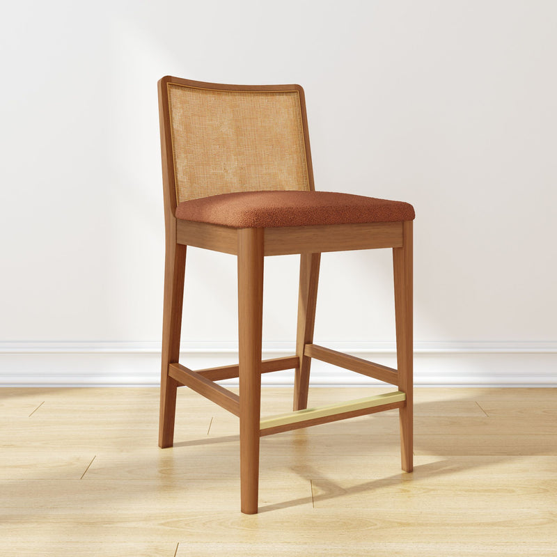 Mid-century modern wooden counter-height bar stool with cane back, rust upholstered seat and brass footrest on light hardwood floor