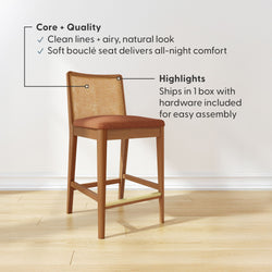 Mid-century modern wooden counter-height bar stool with woven cane back, rust bouclé seat cushion and brass footrest on light wood floor, showcasing clean lines and natural look