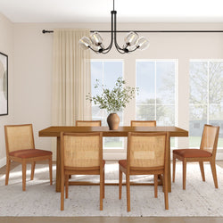 Modern dining room with wooden table, six cane-back chairs, glass pendant light, vase of greenery and large windows