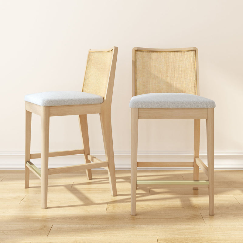 Pair of counter-height light wood bar stools with rattan cane backs and beige upholstered seats on hardwood floor — modern Scandinavian kitchen island seating