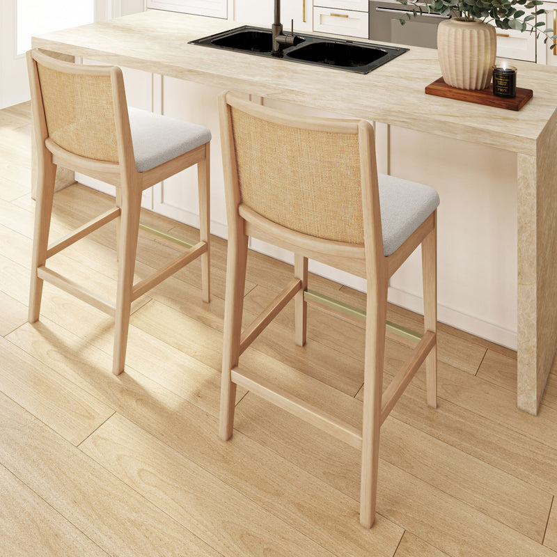Two light wood counter-height bar stools with woven cane backs and gray upholstered seats at a modern kitchen island on light oak flooring