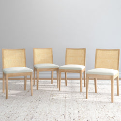 Four modern wooden dining chairs with beige cushions against a neutral background.