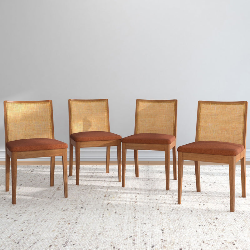 Four wooden dining chairs with woven backs and orange cushions on a beige carpet.