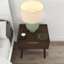 Mid-century modern bedside table with lamp, book, and candle in bedroom setting.