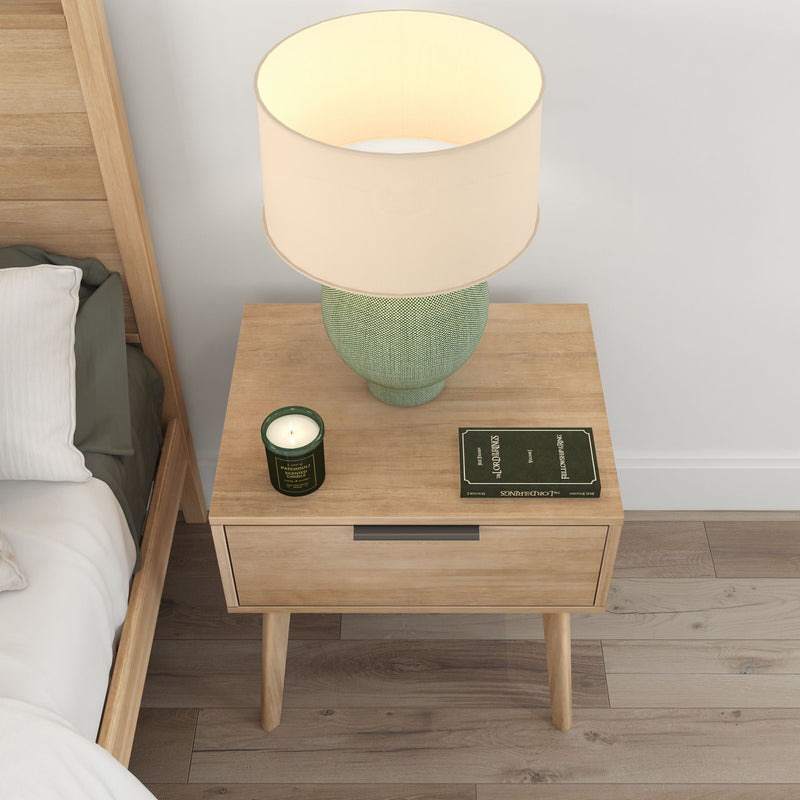 Wooden bedside table with a modern lamp, candle, and book in a cozy bedroom setting.
