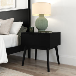 Black mid-century modern nightstand with green ceramic table lamp, scented candle and book beside white bed in minimalist bedroom