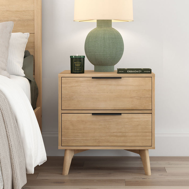 Beige wooden nightstand with a modern design beside a bed, featuring a decorative lamp, green candle, and book for stylish bedroom decor.