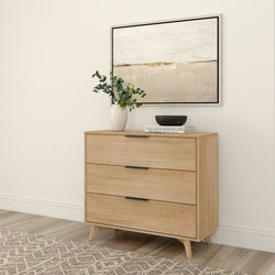 Mid-century modern wooden dresser with three drawers, decorative vase, books, and abstract wall art in a minimalist room setting.