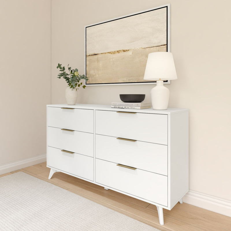 Minimalist white dresser with modern decor, featuring a vase with greenery, books, and a lamp, beneath a neutral abstract painting.