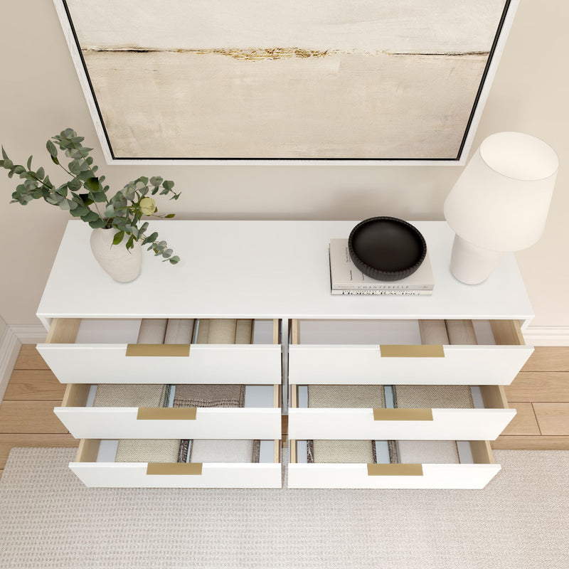 Modern white dresser with open drawers displaying neatly folded clothes, topped with a vase, lamp, and decorative items.