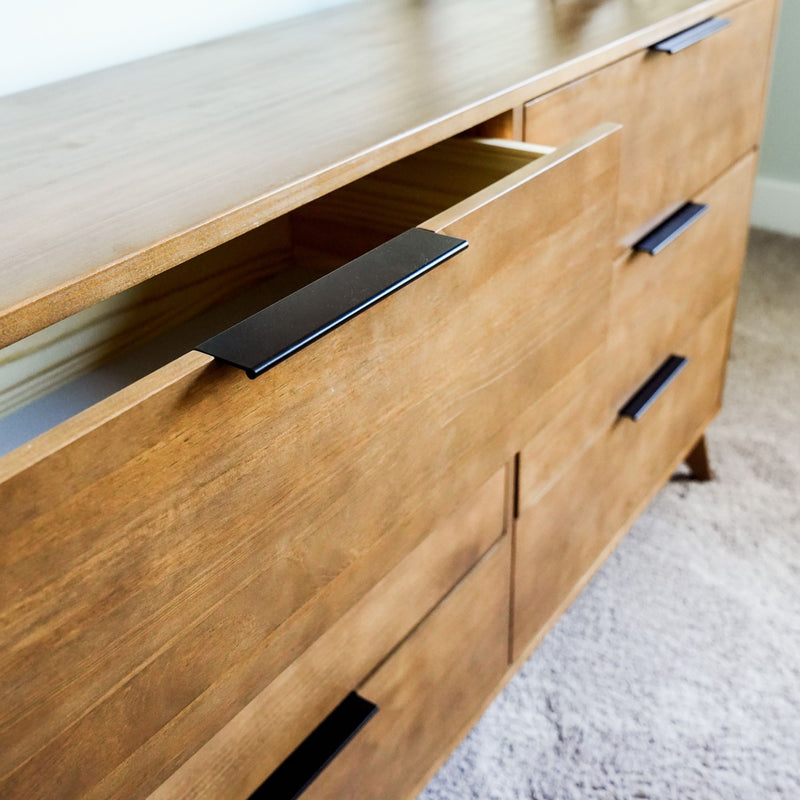 Mid-century modern walnut dresser with black metal drawer pulls, partially open drawer on carpeted bedroom floor