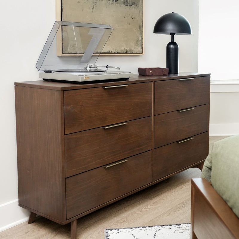 Mid-century modern wooden dresser with record player and black lamp in stylish bedroom interior.
