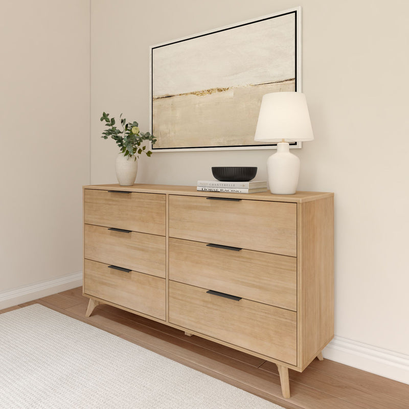 Modern wooden dresser with drawers in a minimalist bedroom, featuring a lamp, decorative vase, and abstract wall art.