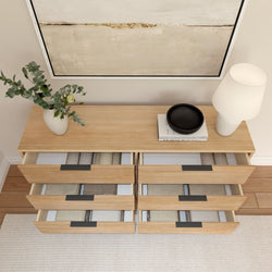 Modern wooden dresser with open drawers, decorative vase, books, and table lamp in a minimalist living room setting.