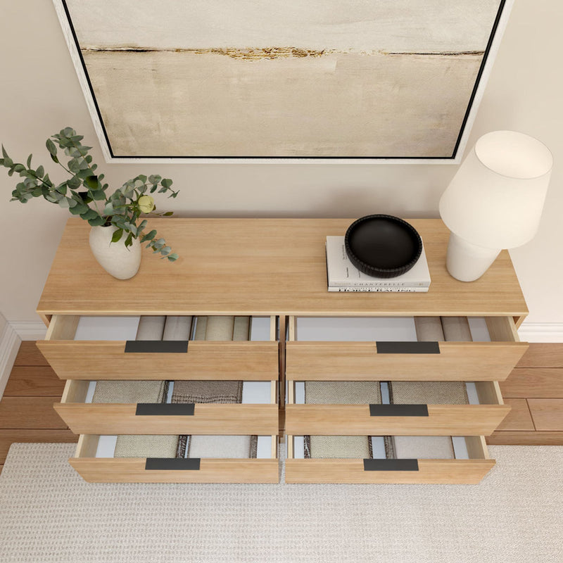 Modern wooden dresser with open drawers, decorative vase, books, and table lamp in a minimalist living room setting.