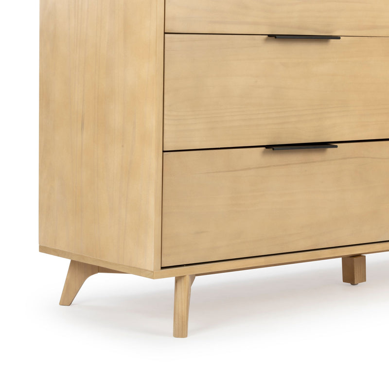 Close-up of light wood mid-century modern dresser with tapered legs, black metal drawer pulls, and smooth wood grain finish