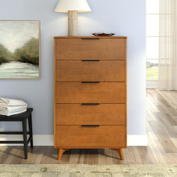 Mid-century modern tall five-drawer wooden dresser in warm walnut finish with black bar pulls, lamp and framed art on hardwood bedroom floor