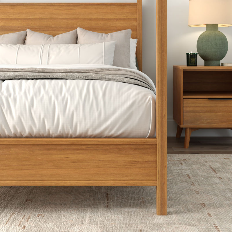 Mid-century modern bedroom interior with natural wood four-post bed frame, crisp white duvet and pillows, matching wood nightstand with lamp and candle on a textured area rug