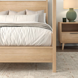 Light wood four-poster bed with white and beige bedding, mid-century nightstand, green ceramic lamp and neutral area rug