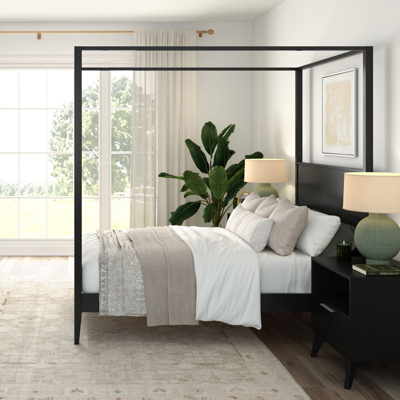 Sunlit modern bedroom with black canopy bed, neutral linens and throw, matching nightstands with lamps, large window with sheer curtains and potted plant