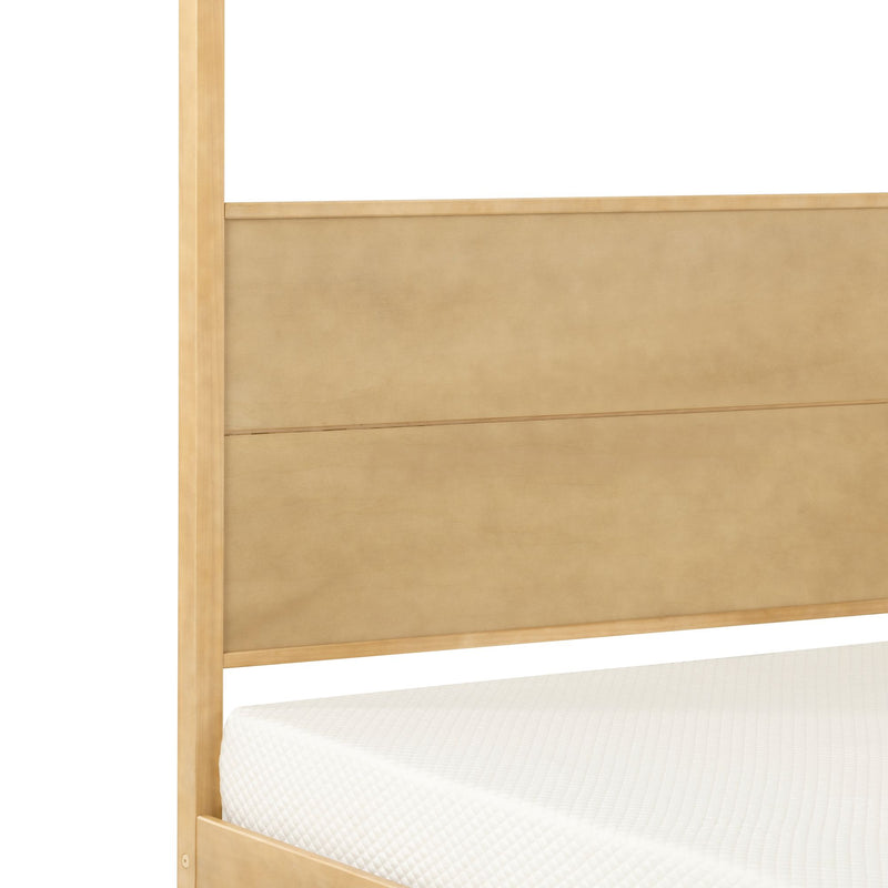Close-up of light wood canopy bed frame with beige upholstered paneled headboard and white quilted mattress