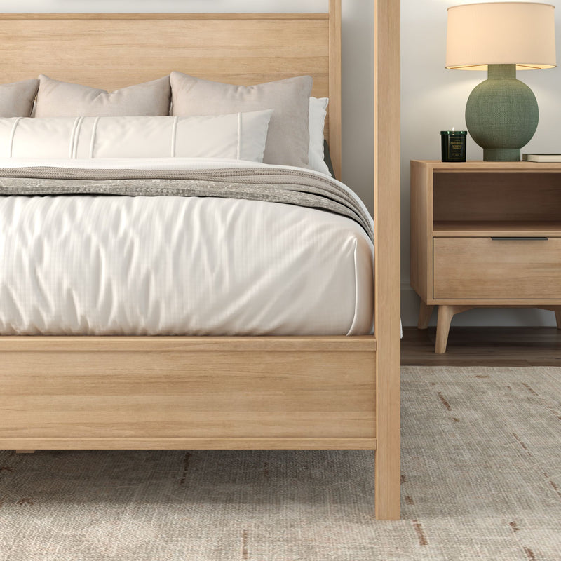 Modern light wood bed frame with neutral linen bedding, textured gray throw and pillows next to a wooden nightstand with green ceramic lamp and scented candle — minimalist Scandinavian bedroom.