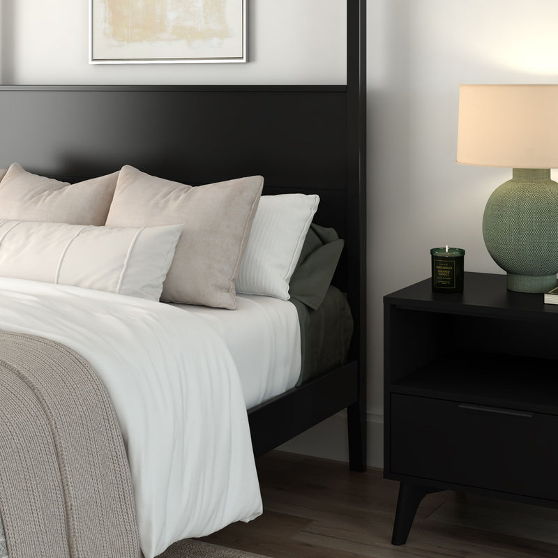 Cozy modern minimalist bedroom with black platform bed, layered white and beige bedding, knit throw, and black nightstand with green ceramic lamp and scented candle.