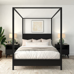 Modern minimalist master bedroom with black four-poster canopy bed, neutral bedding, matching nightstands, table lamps and potted plant.